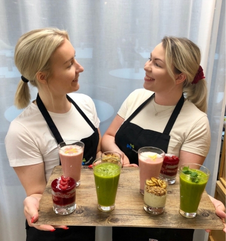 Opiskelijat katsovat toisiaan hymyillen ja ojentavat smoothietarjotina kameralle.