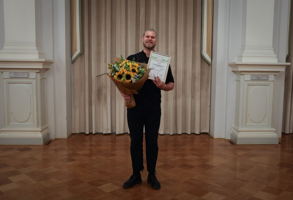 Valtteri Sinkkonen hymyilee kukkien ja voittajan todistuksen kanssa.
