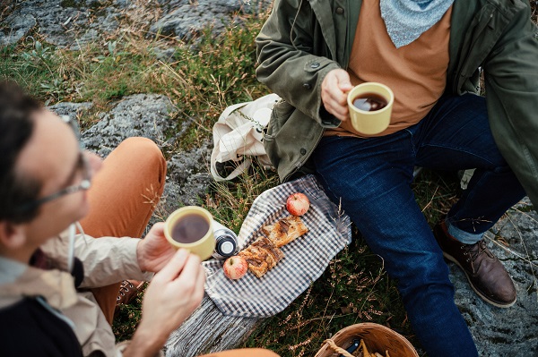 Kaksi henkilöä juo kahvia kalliolla. Viltin päällä palat omena-piirakkaa.